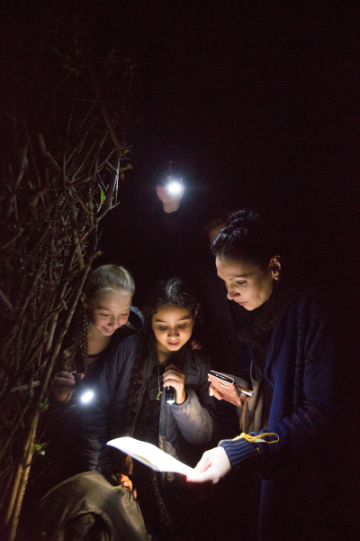 Une famille éclaire avec des lampes un document pour un jeu de piste nocturne dans le labyrinthe géant des Jardins de Colette