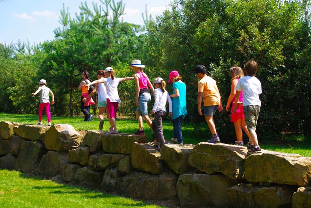 un groupe d'enfants se promènent sur un muret de gros blocs de granite aux Jardins de Colette